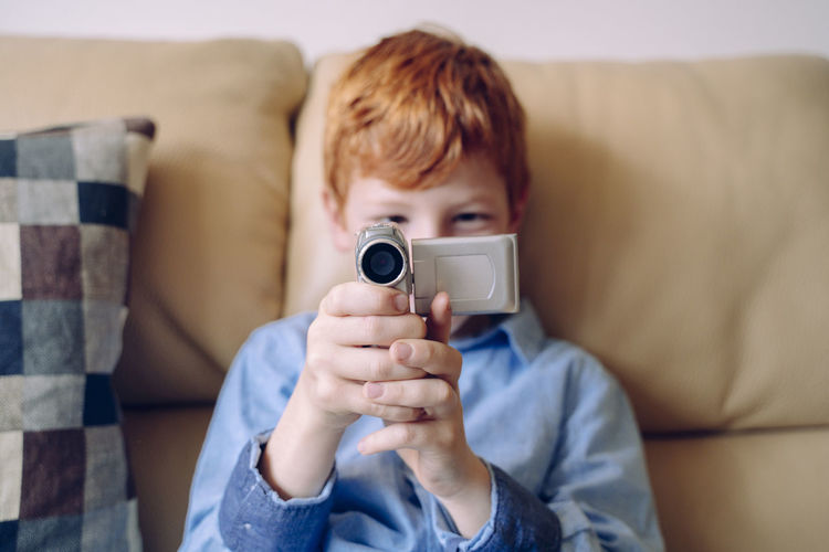 Portrait of boy holding camera while sitting on sofa