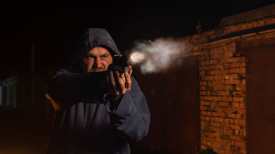 Man wearing hood shooting pistol