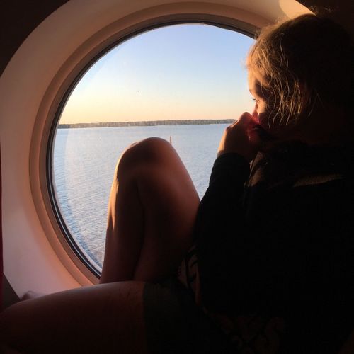 Girl looking at sea through porthole of ship