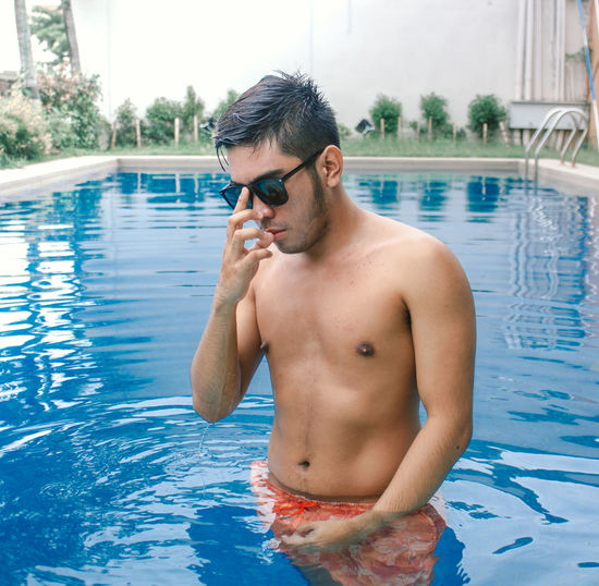 Young shirtless man standing at swimming pool