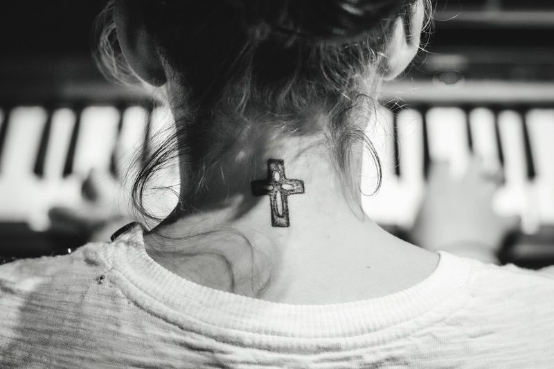 Rear view of woman playing piano with cross on neck