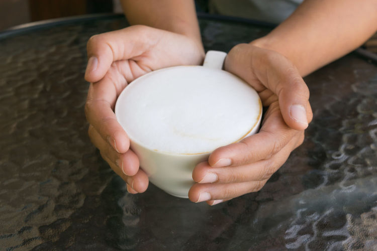 Cropped image of person holding frothy drink at table