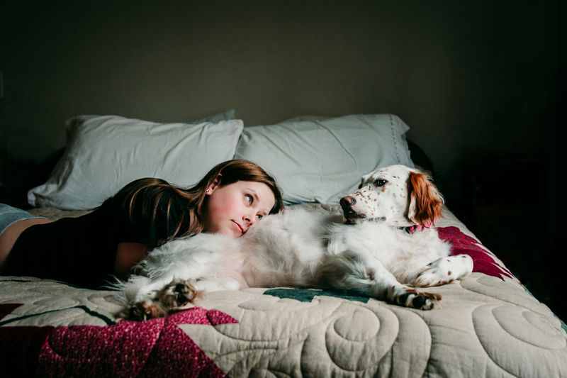 Teenager girl lying down with dog on bed
