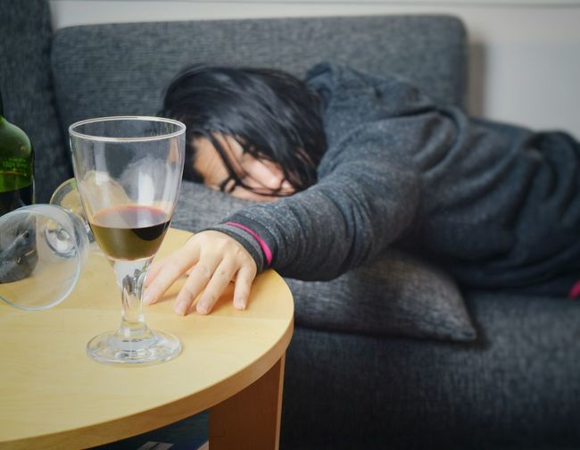 Side view of drunk woman lying down by wineglass on sofa at home