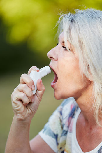 Close-up of senior woman spraying asthma inhaler