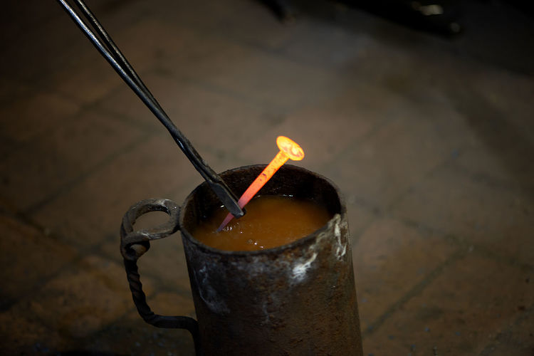 Blacksmith with working tools puts a hot melal nail in the water