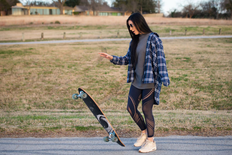 Full length of young woman with skateboard standing on road