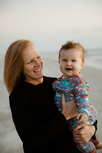 Young redhead mom laughs and holds laughing fat baby boy in onesie