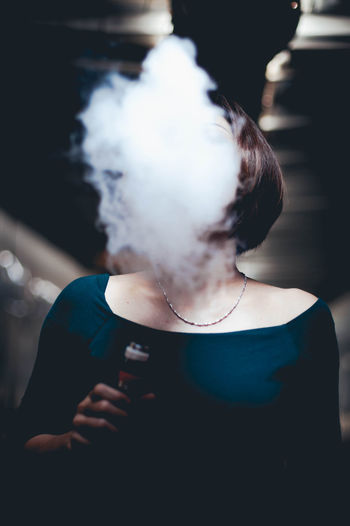 Woman exhaling smoke while holding electronic cigarette