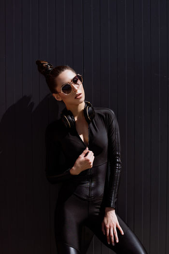 Young woman wearing sunglasses while standing against wall
