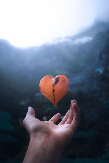 Cropped hand levitating heart shape leaf against rock formations