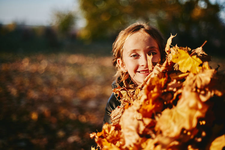 Portrait of girl by stack of autumn leaves