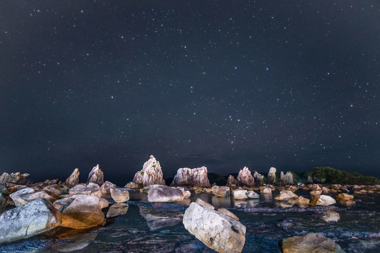 Rocks by sea against sky at night