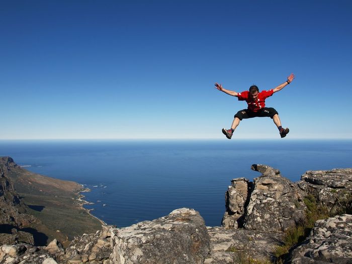 Man jumping over sea against clear blue sky