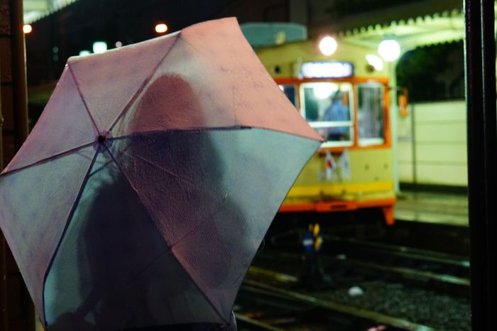 Rear view of woman with umbrella standing at railroad station
