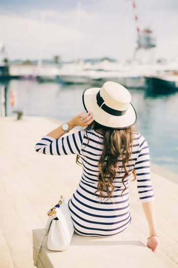 Rear view of woman in hat sitting at harbor