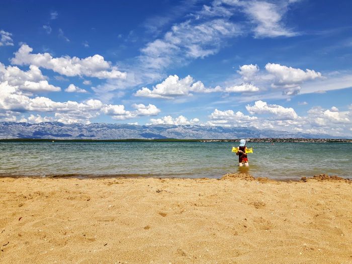 Boy standing in sea water against sky