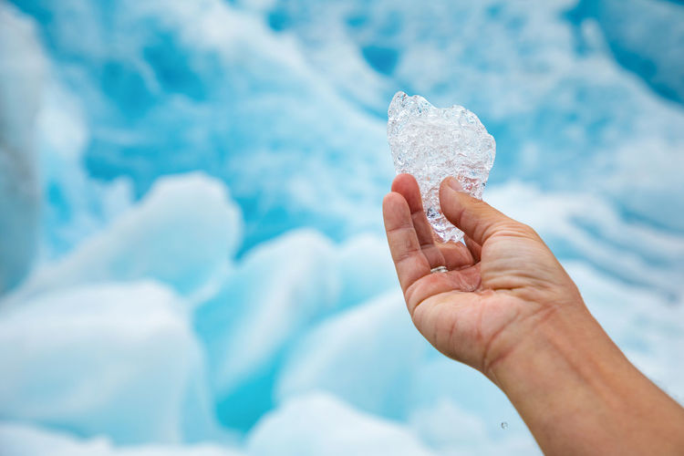 Cropped image of person hand holding ice against icebergs