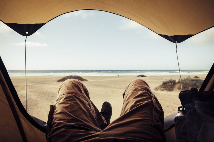 Low section of person relaxing in tent at beach