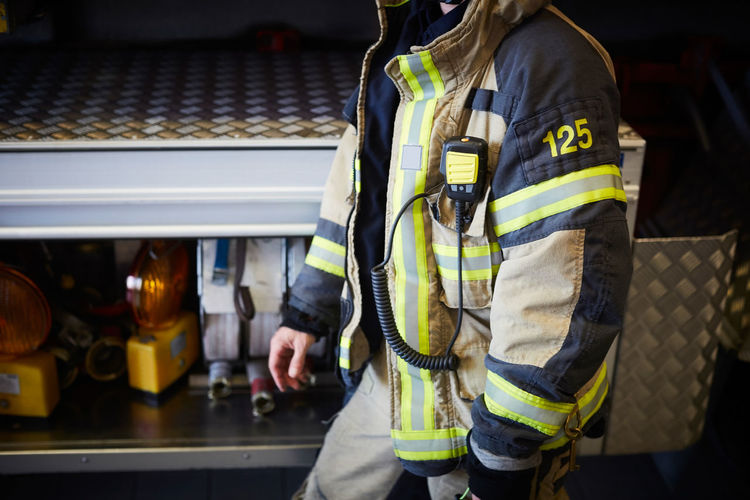 Midsection of firefighter with walkie-talkie walking at fire station