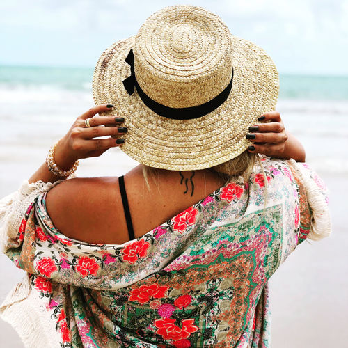 Rear view of woman wearing hat standing on beach
