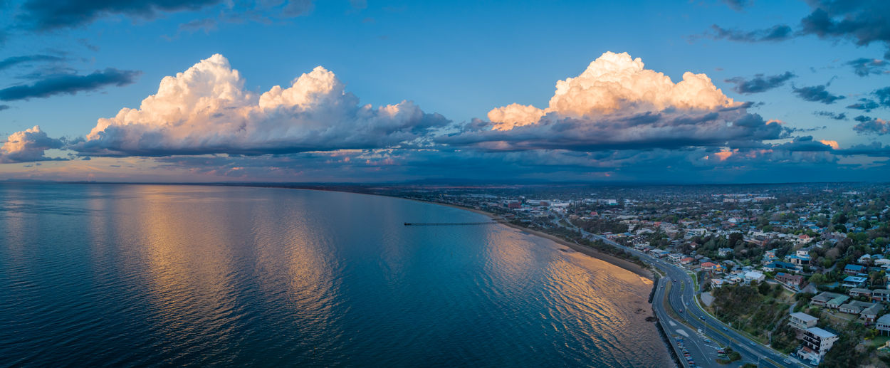Panoramic shot of sea and cityscape against cloudy sky