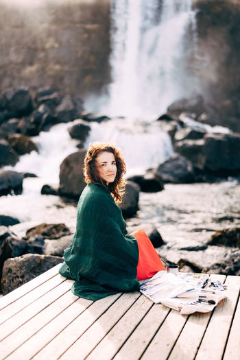 Portrait of woman sitting on rock by water