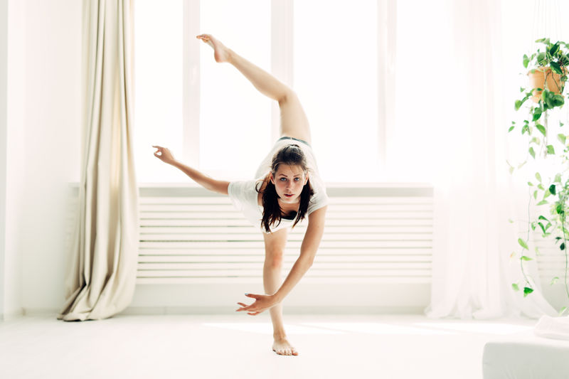 Full length portrait of young woman practicing yoga in warrior position at home