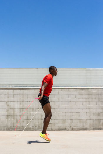 Side view of energetic african american male athlete skipping rope above ground while doing exercises during training in summer