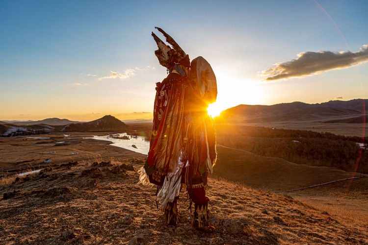 Mongolia shaman holding drum doing authentic ritual of summoning spirits.sunset moment