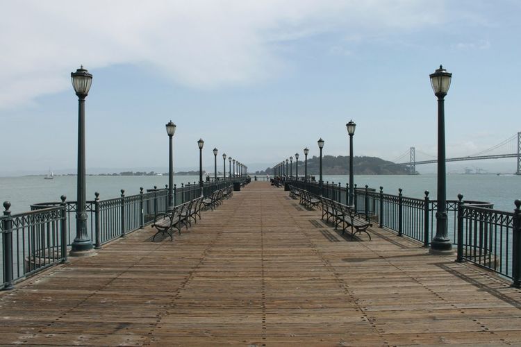 Row of benches and gas lights on pier against sky