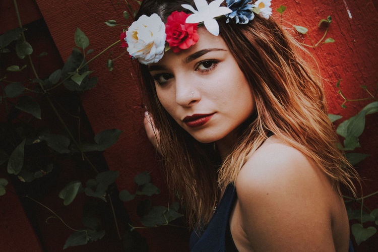 Close-up portrait of beautiful young woman wearing flowers against wall