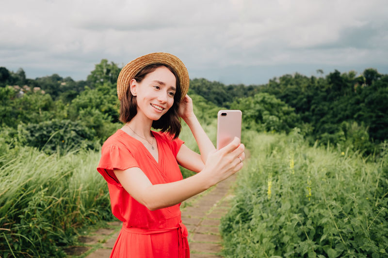 Smiling young woman using phone while standing on plants