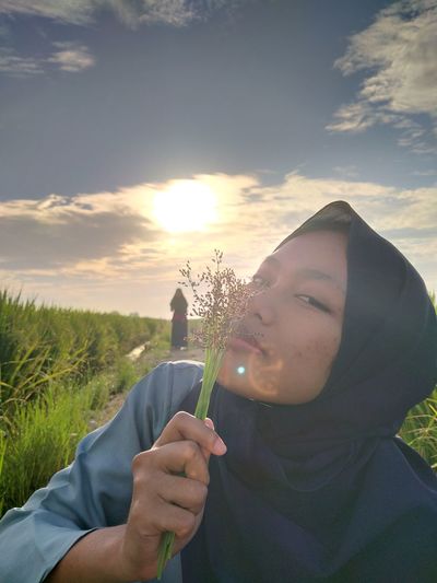 Portrait of woman holding flowers on field against sky during sunset