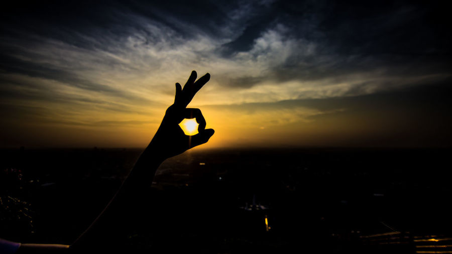 Silhouette hand gesturing ok sign against sky during sunset