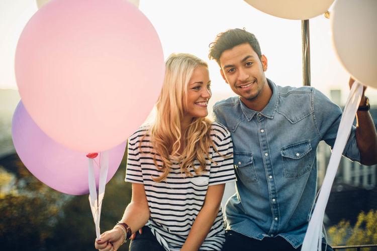 Couple sitting with balloons against sky