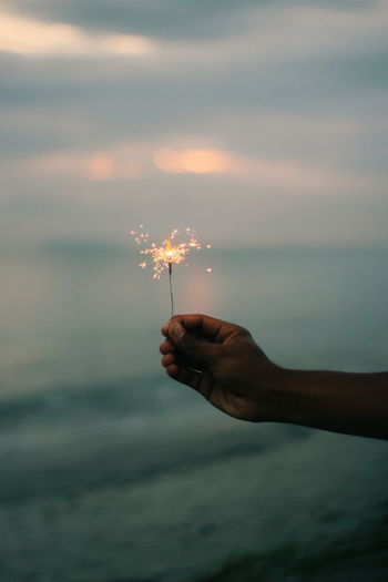 Person holding fishing rod over sea against sky