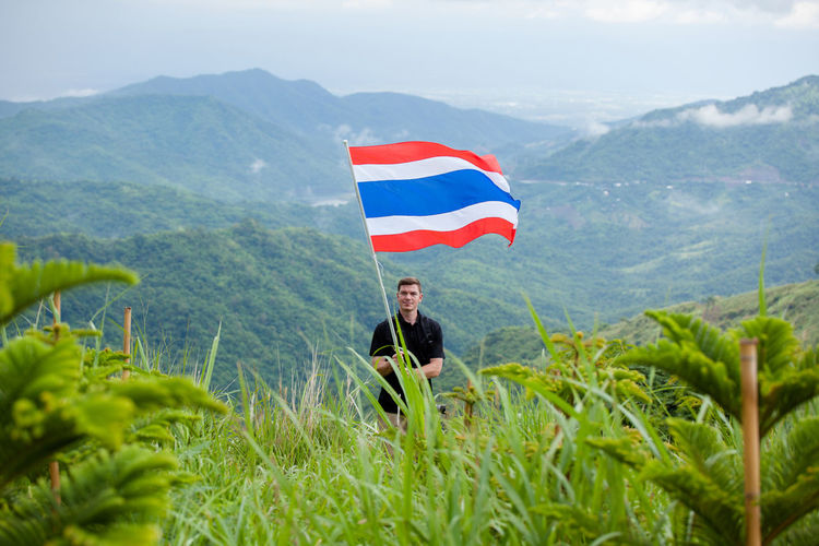 Man with thai flag standing on field against mountains