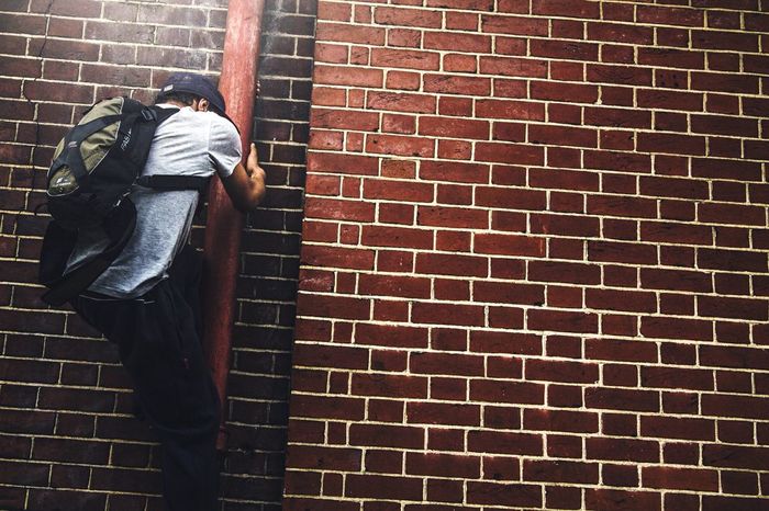 Man climbing pipe against brick wall