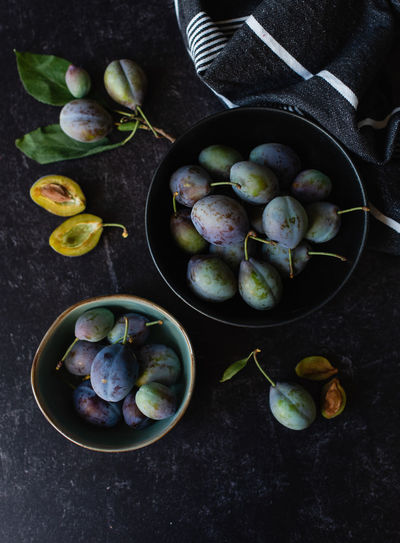 Overhead shot of bowls of fresh plums against a black background.
