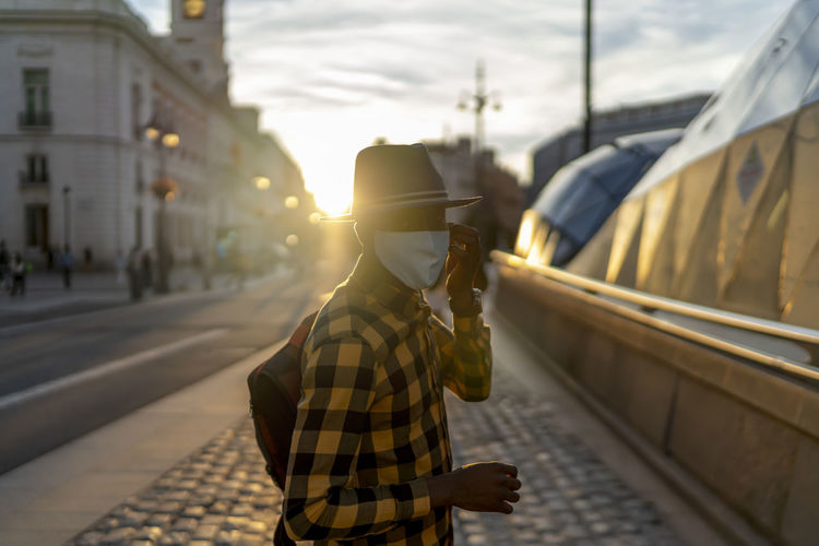 African man wearing protective face mask on sidewalk during sunset