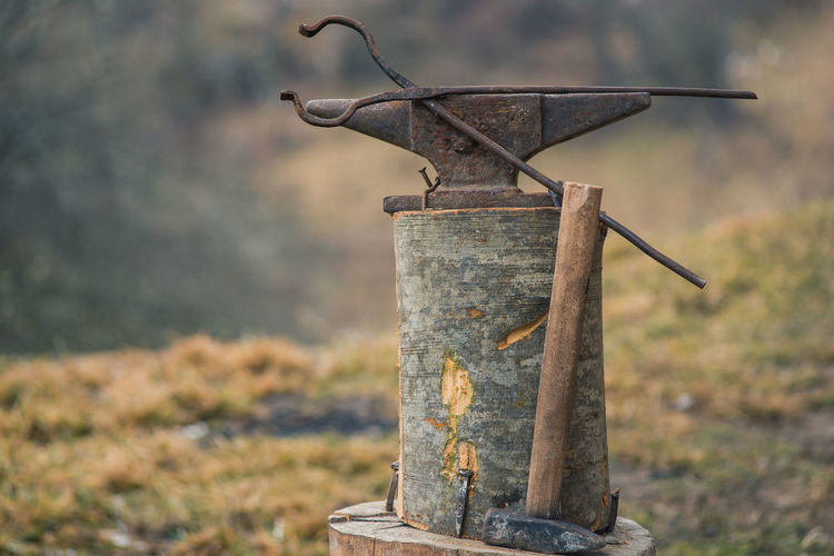 Bolt tongs and a hammer near a old rusty anvil outdoors with blurry background