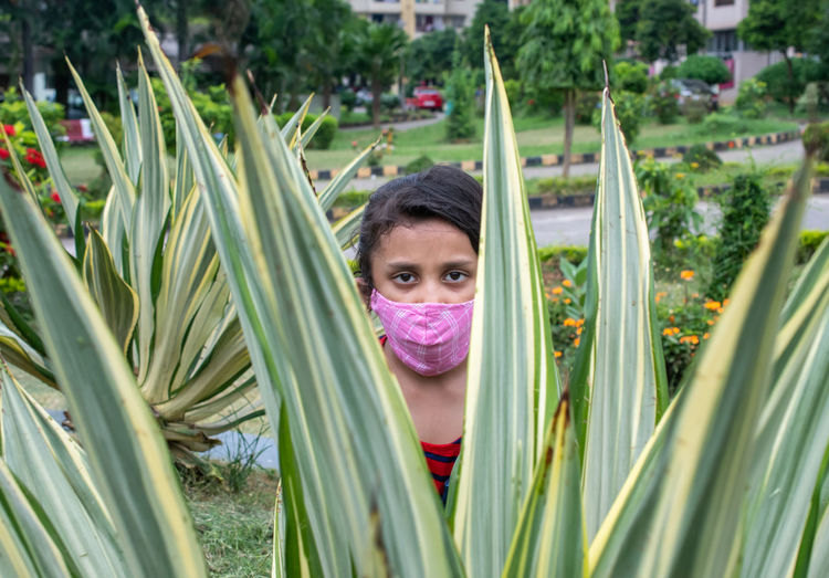 Closeup of girl wearing face mask through leaves of plant