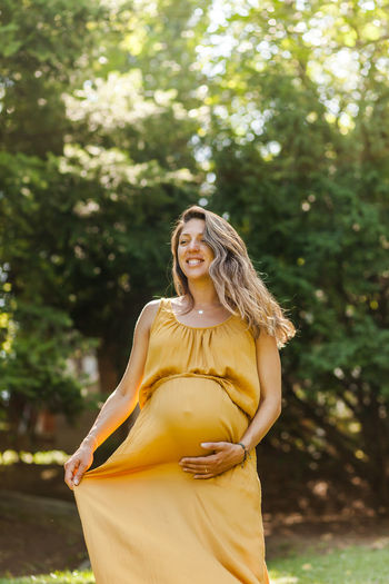 Pregnant woman holding stomach while standing outdoors