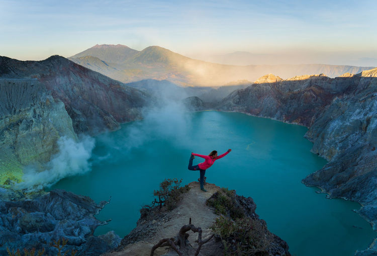 High angle view of woman exercising on cliff against lake