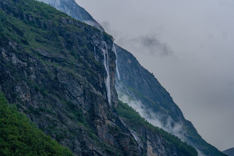 Low angle view of rocky mountains and waterfall against sky