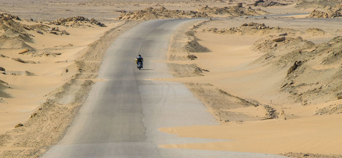 Rear view of man riding motorcycle on road at desert