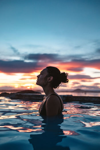 Woman standing by swimming pool in sea against sky during sunset