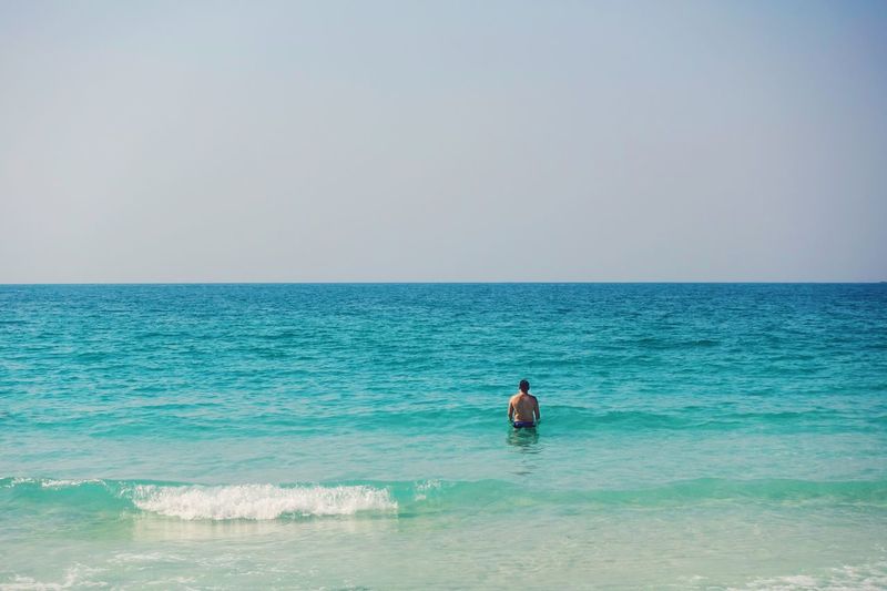 Rear view of man standing in sea against clear sky