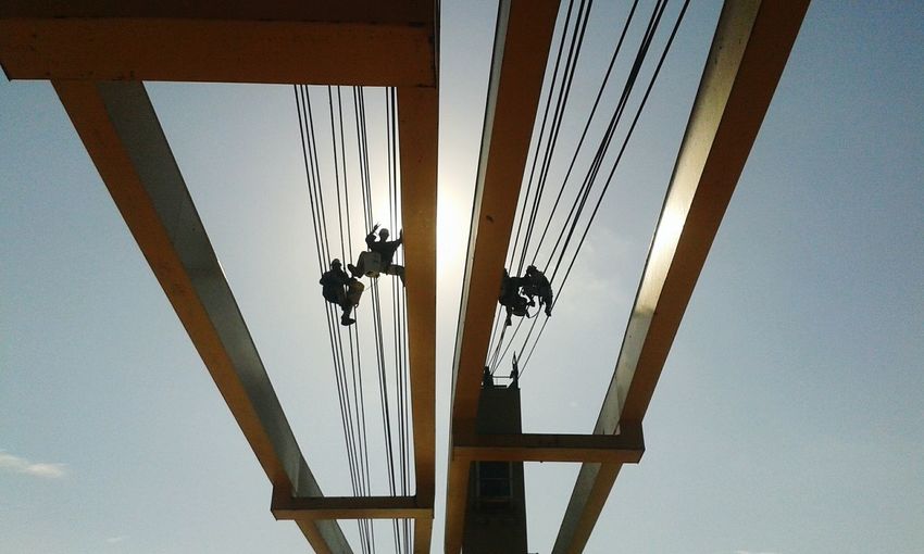 Low angle view of workers on steel cable at bridge against sky